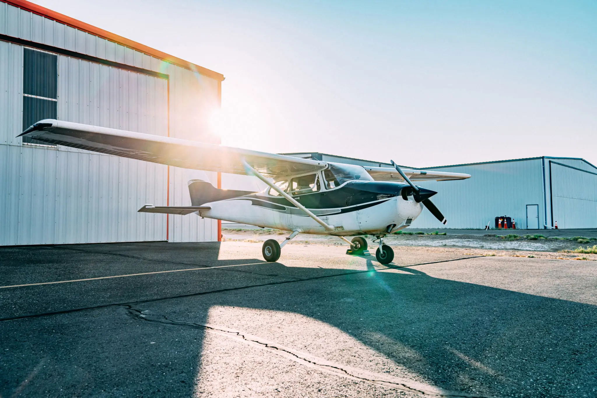 Small propeller airplane parked near a hangar with sunlight.